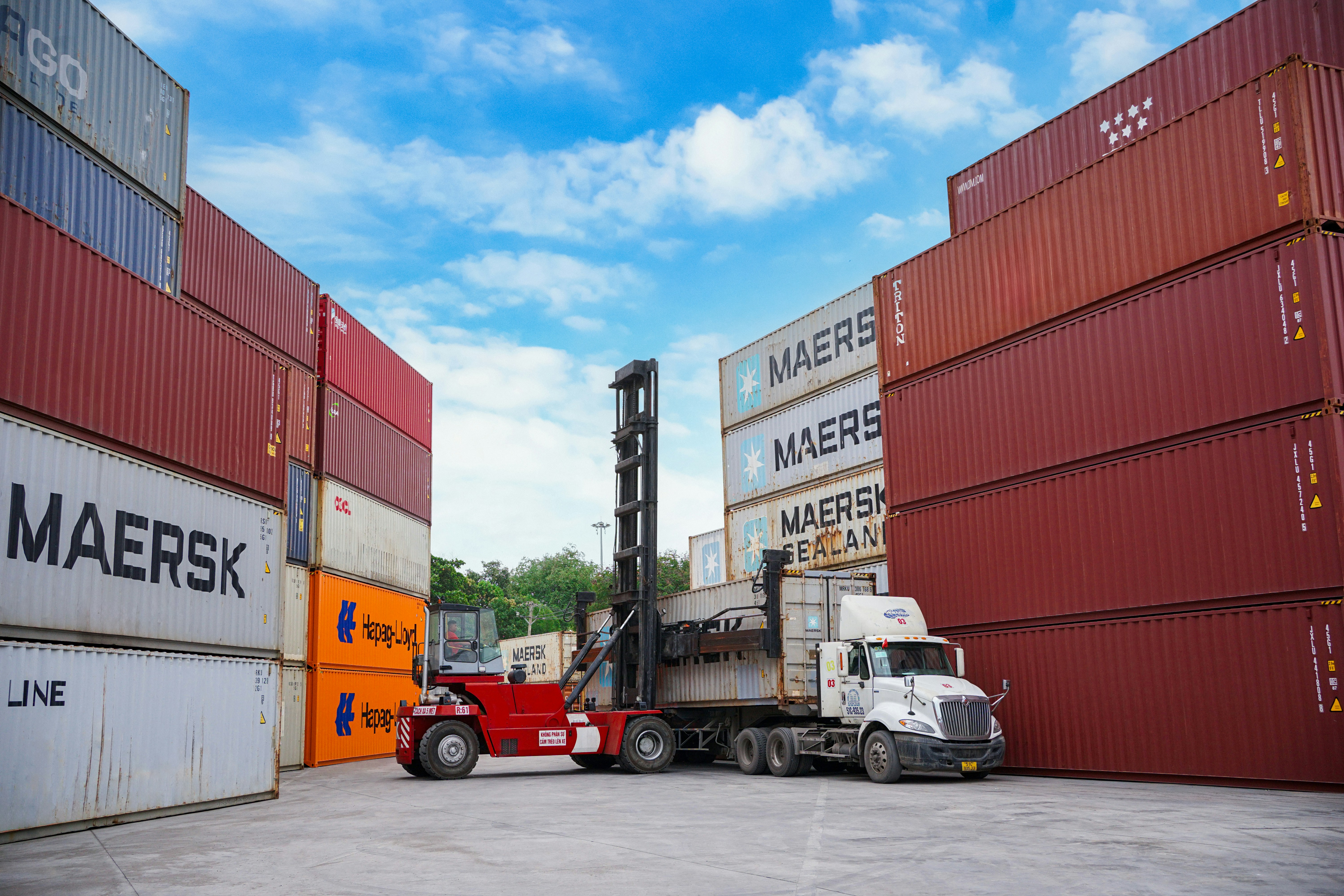 A container yard with a truck, forklift, and stacked shipping containers